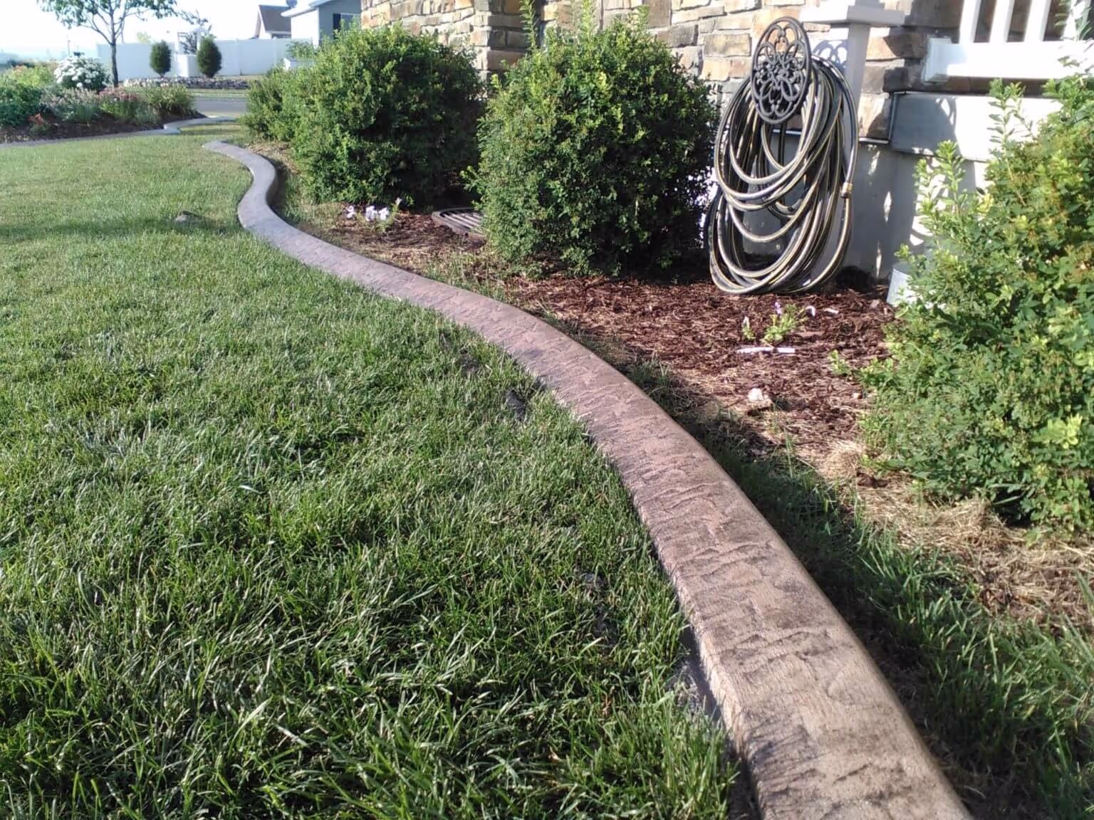 Curved stamped concrete curbing separating lawn from mulched garden bed in Providence, Utah