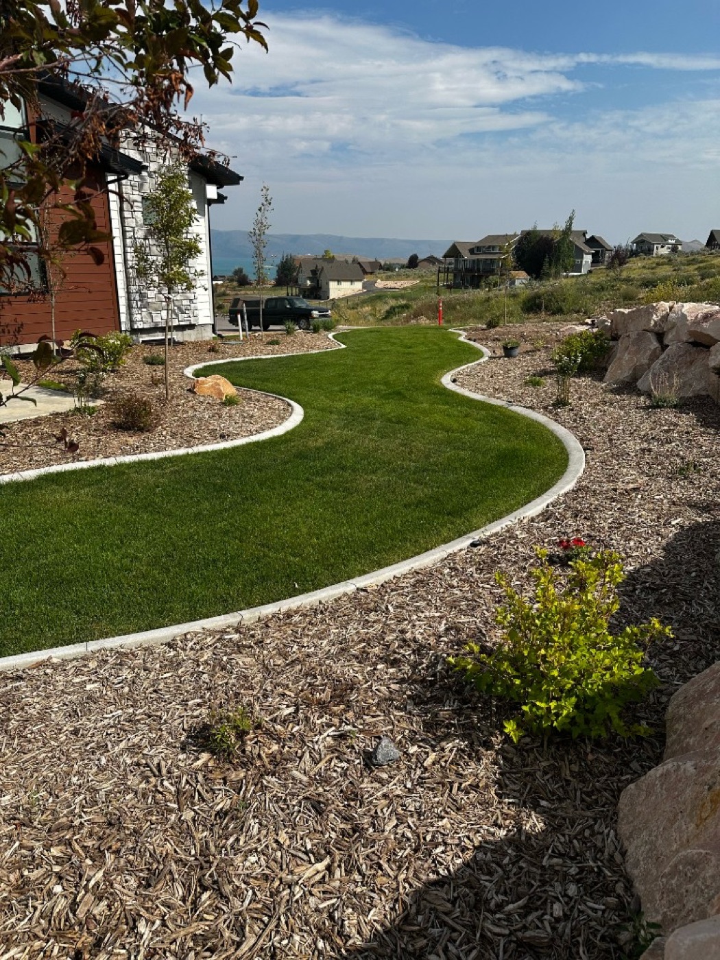 Winding S-curve concrete curbing separating lawn from mulch beds with lake views in Utah